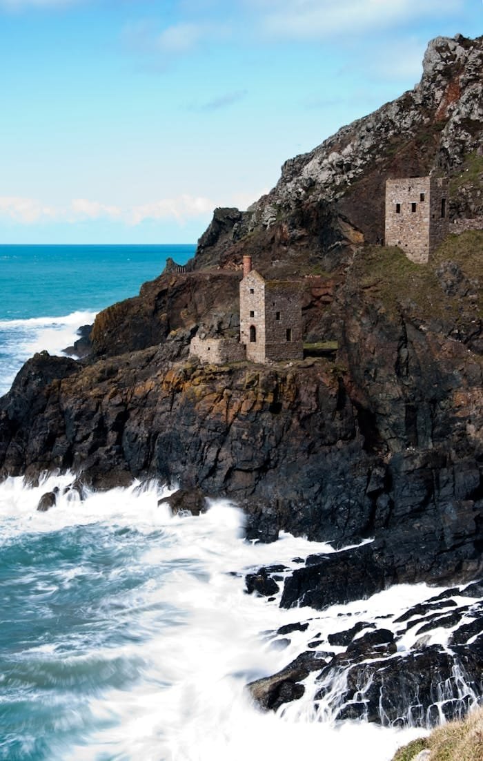 our-story Cornish Engine Houses on the cliffs above crashing waves
